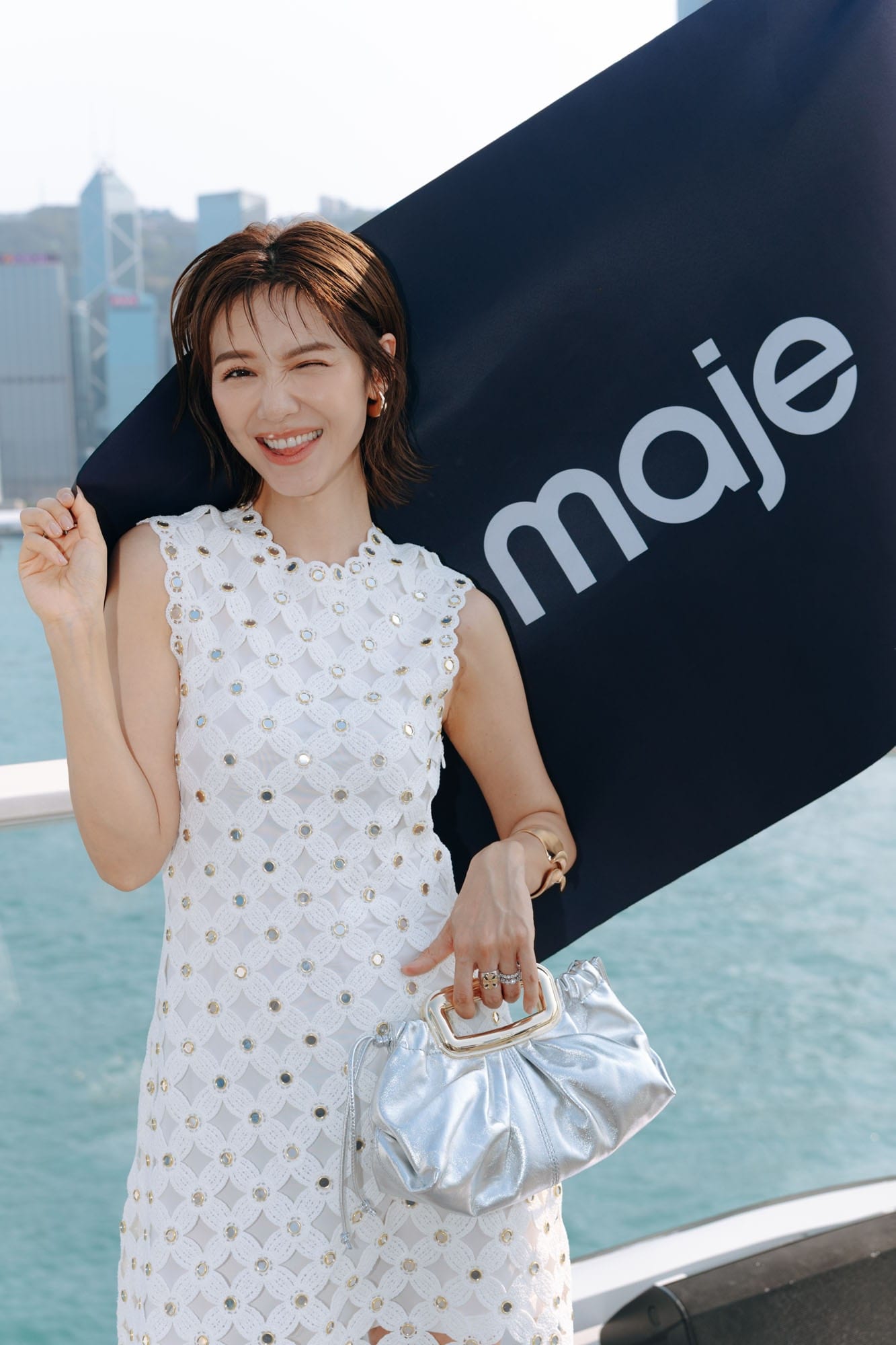 Guest holding a silver Maje bag beside a Maje flag