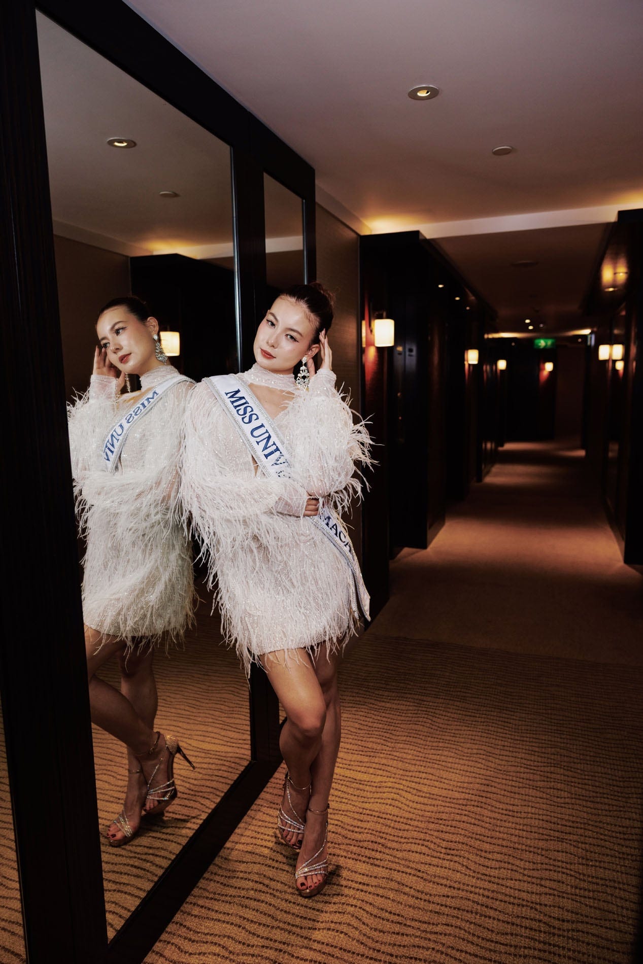Cassandra posing beside her reflection in a hotel corridor
