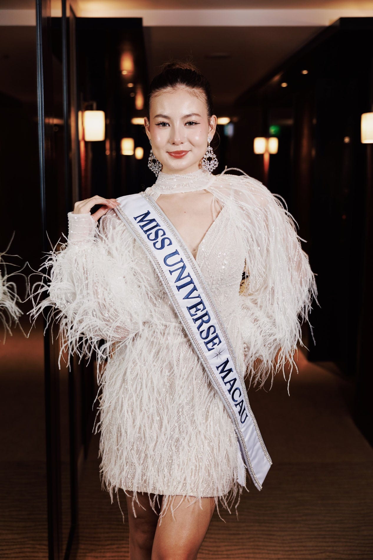 Cassandra in a white feathered dress and Miss Universe sash