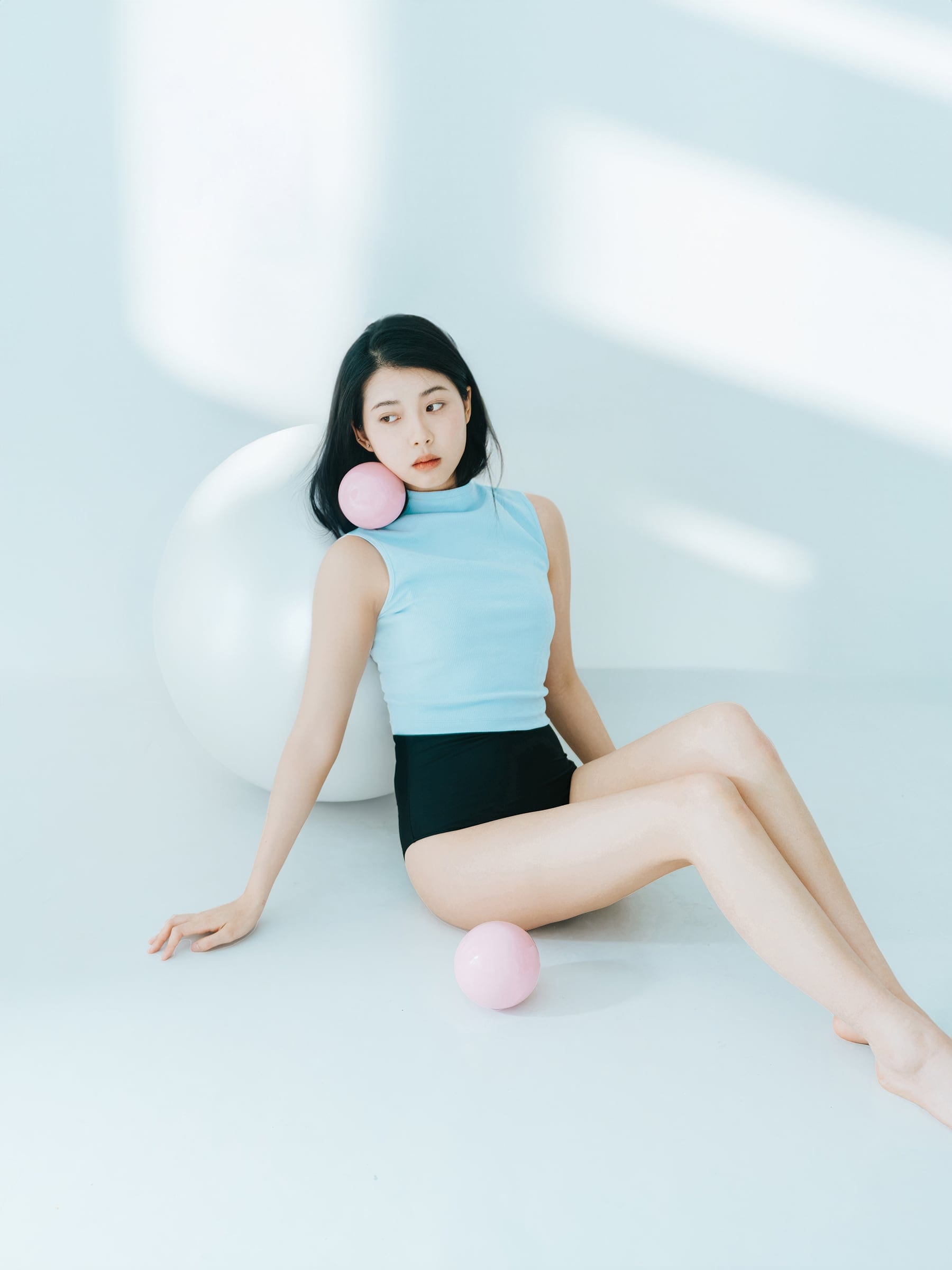 Seated portrait in a pale blue studio with pink spheres
