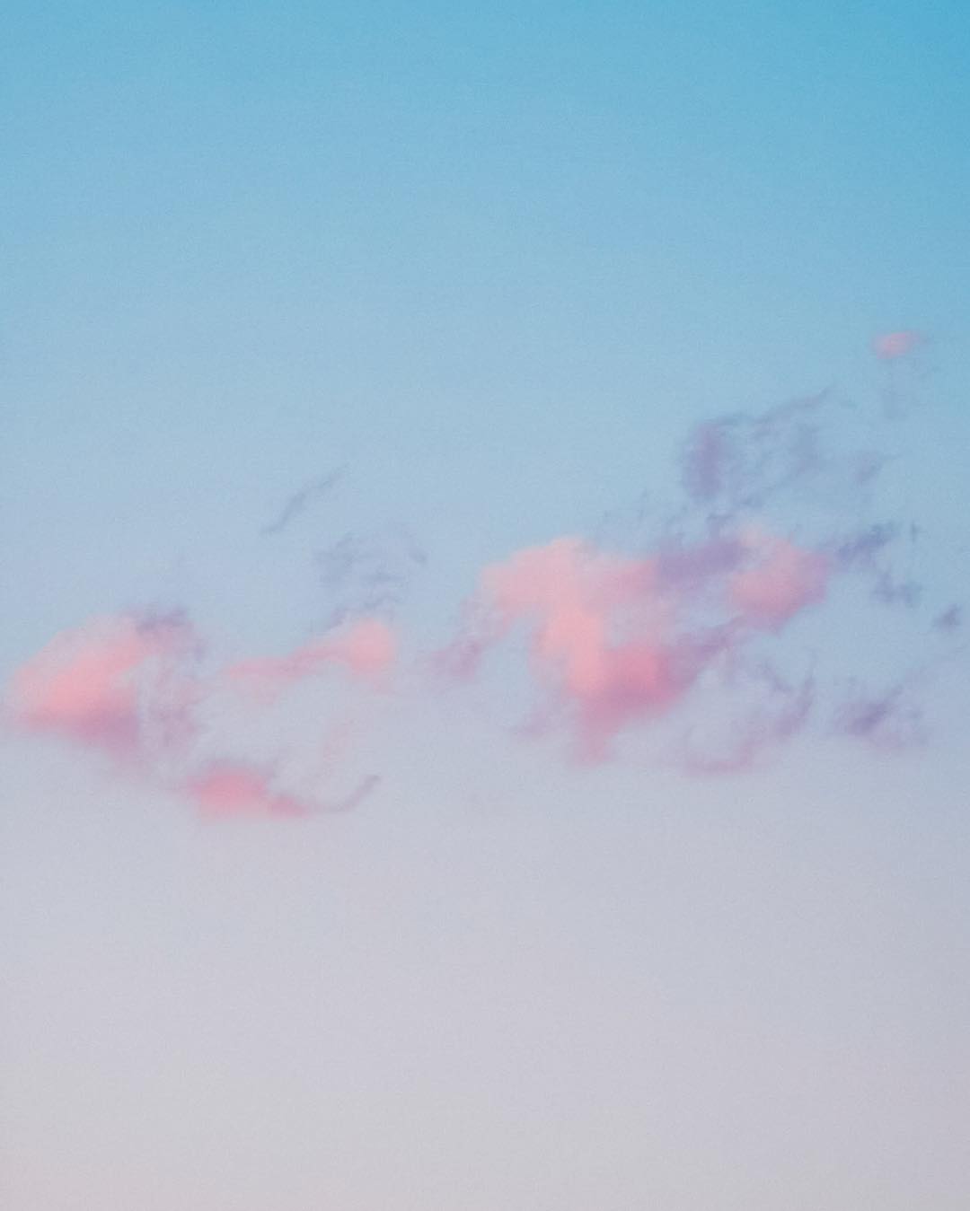 Soft pink clouds floating across a pale blue sky